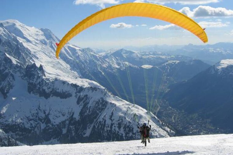 A person is paragliding over a snowy mountain