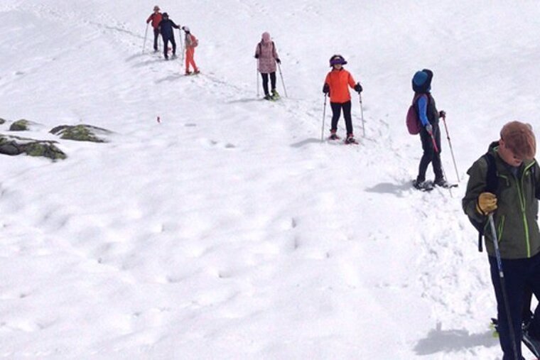 A group of people are snowshoeing down a hill